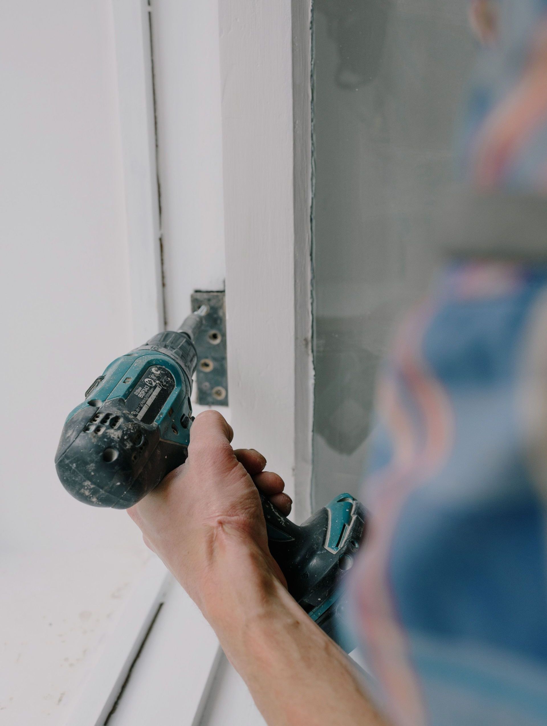Crop bearded guy installing new wooden window with contemporary screwdriver and metal hinge during renovation process in apartment